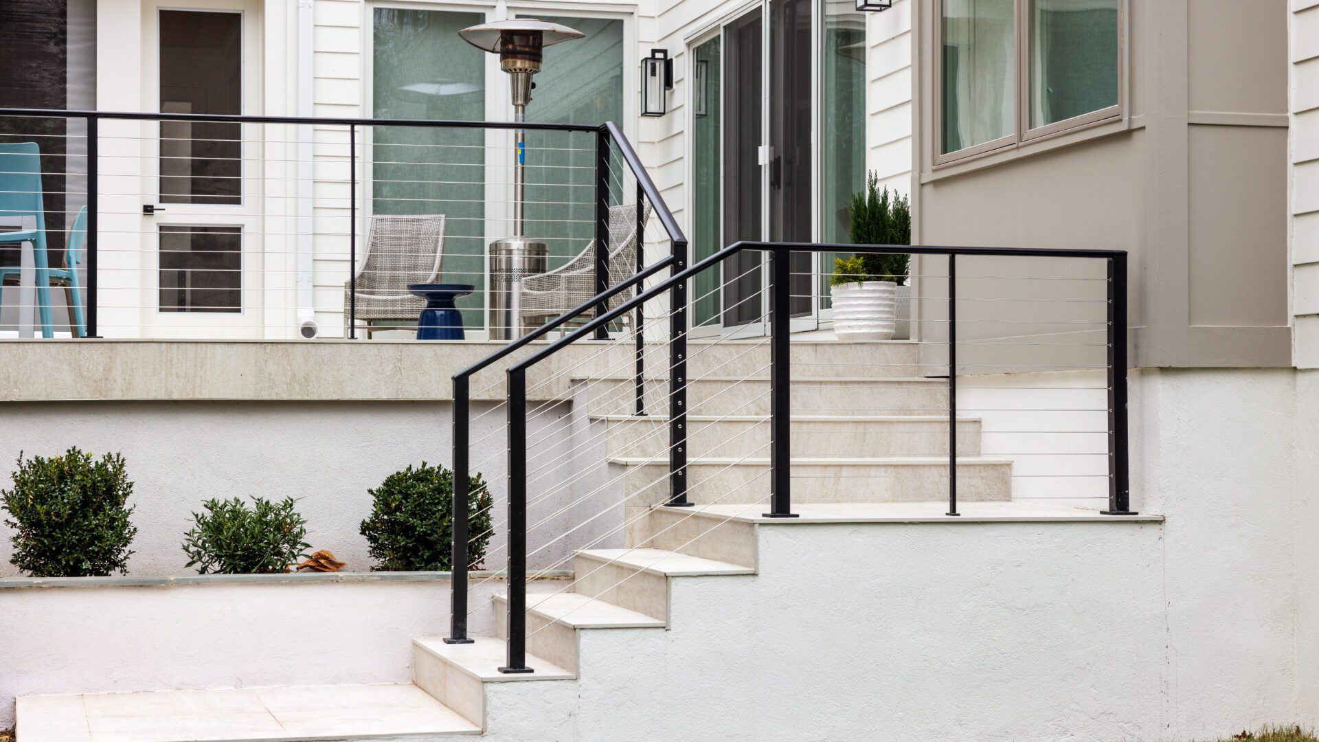Stainless steel cable railing with black powder coated posts and white concrete treads.