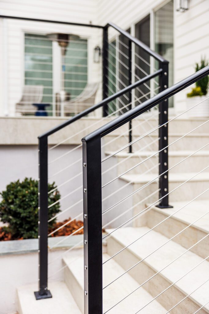 Close detail of a black post and caprail railing with cables passing through the bottom.