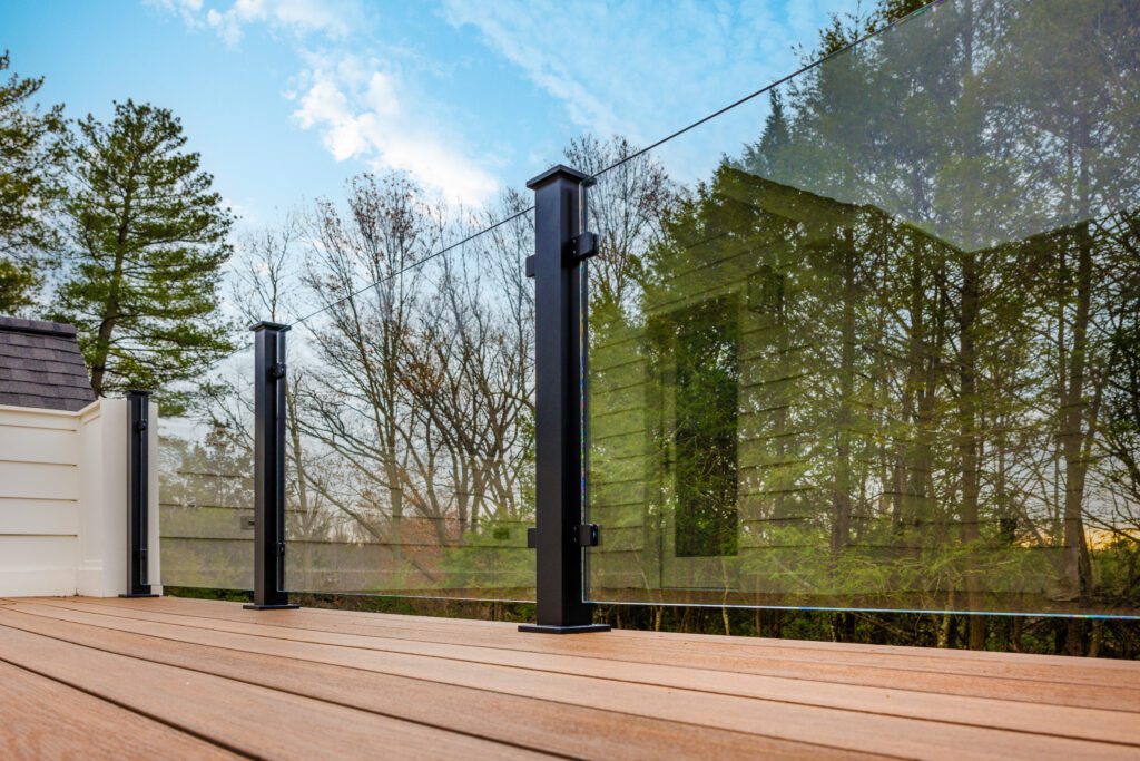 Glass Railing with black posts; back dropped with a bold green treeline.